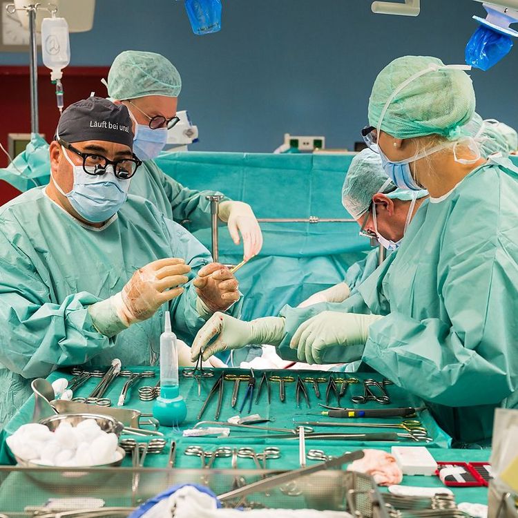 Steriler OP-Saal mit Chirurgieteam bei konzentrierter Arbeit am Operationstisch, mit steriler OP-Kleidung.