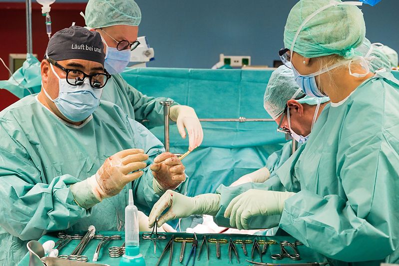 Steriler OP-Saal mit Chirurgieteam bei konzentrierter Arbeit am Operationstisch, mit steriler OP-Kleidung.