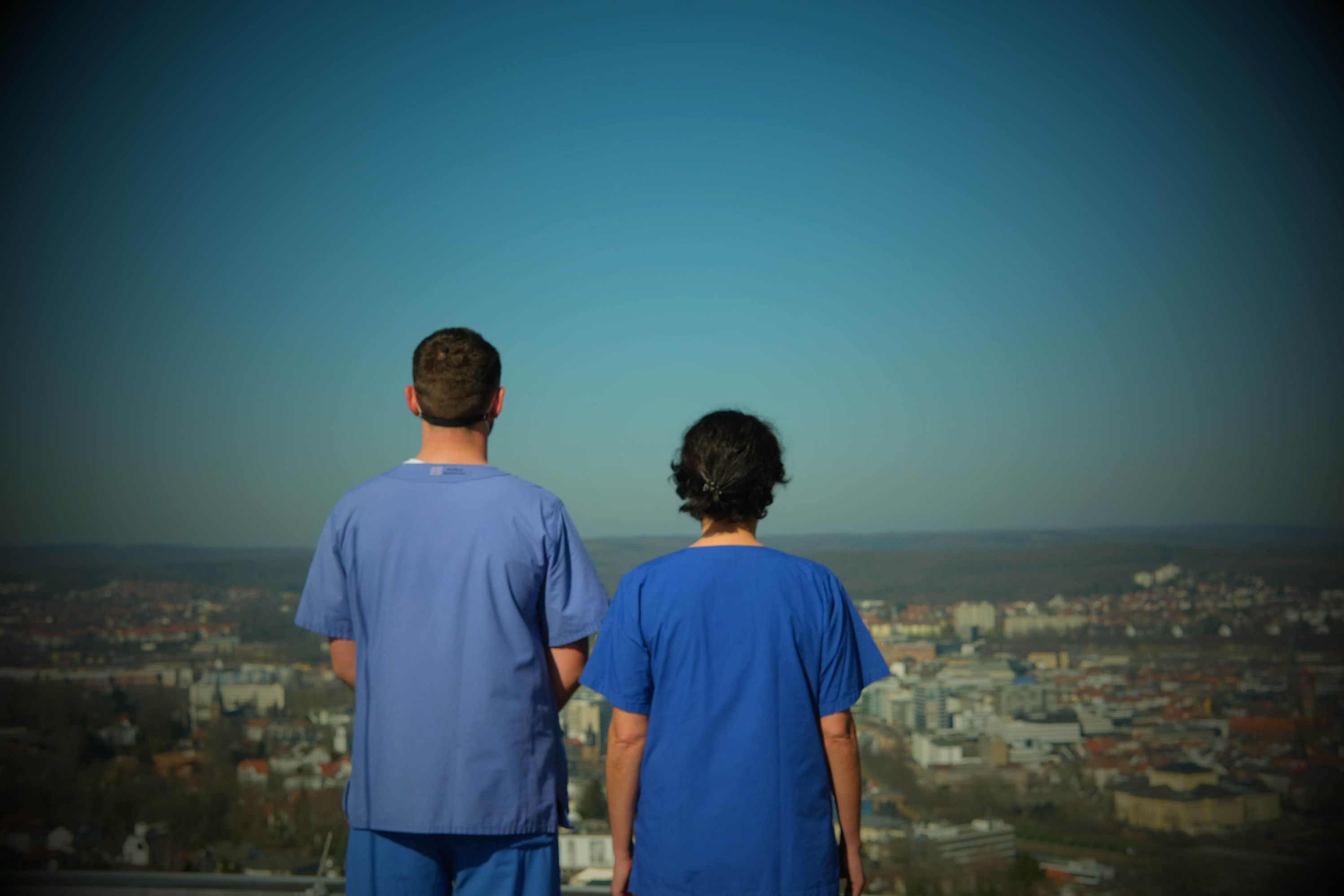 Zwei Pflegefachkräfte blicken vom Dach des Klinikums Saarbrücken auf dem Winterberg auf die Stadt Saarbrücken