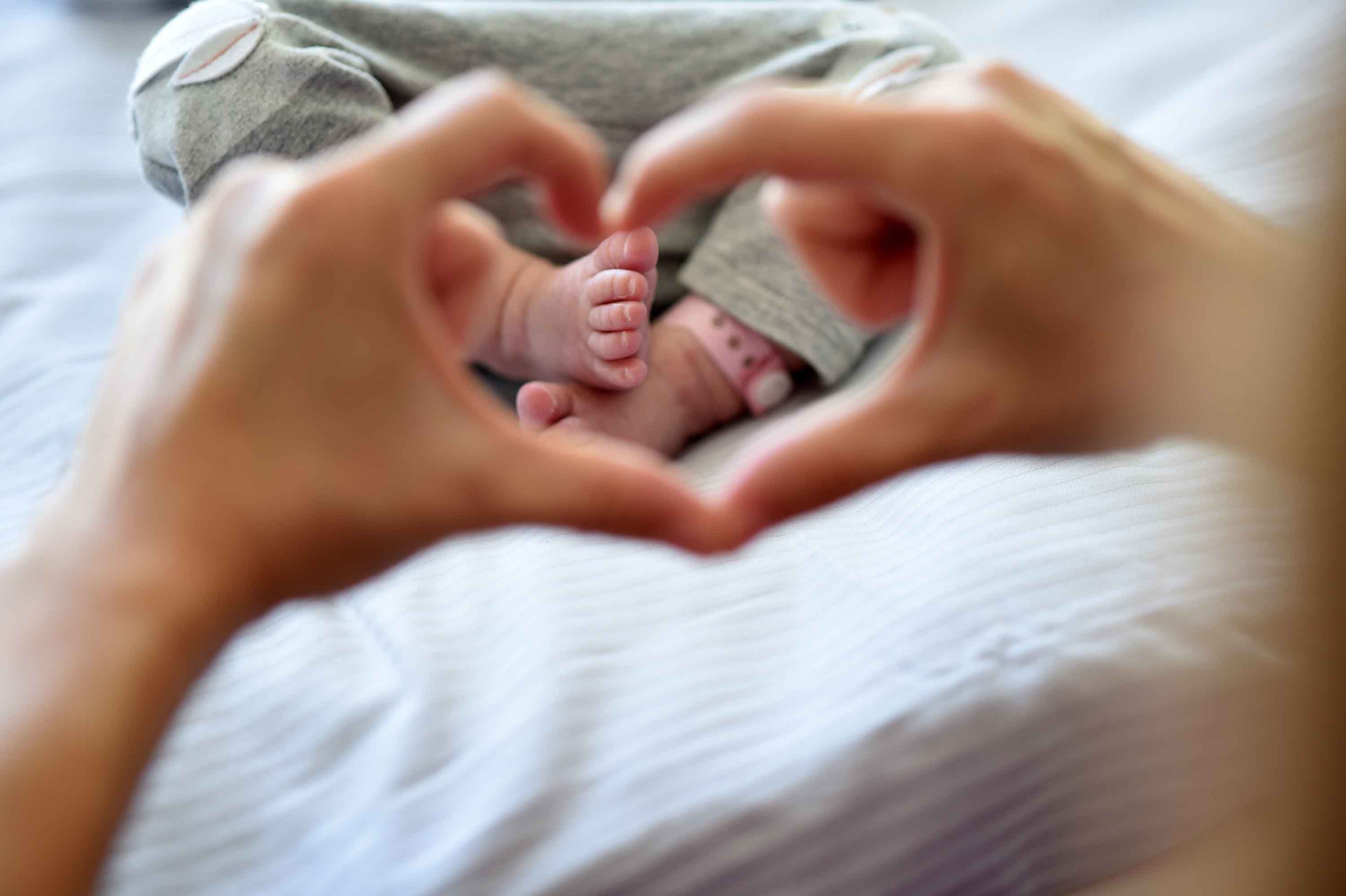 Hände bilden ein Herz um die Füße eines Neugeborenen im Krankenhausbett im Klinikum Saarbrücken