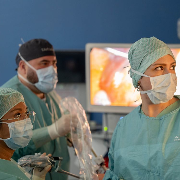 Operationsteam der Allgemeinchirurgie in steriler OP-Kleidung, mit medizinischem Gerät in der Hand, konzentriert nach rechts blickend