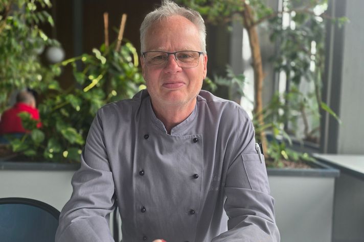 Der Küchenchef sitzt am Tisch und schaut in die Kamera.