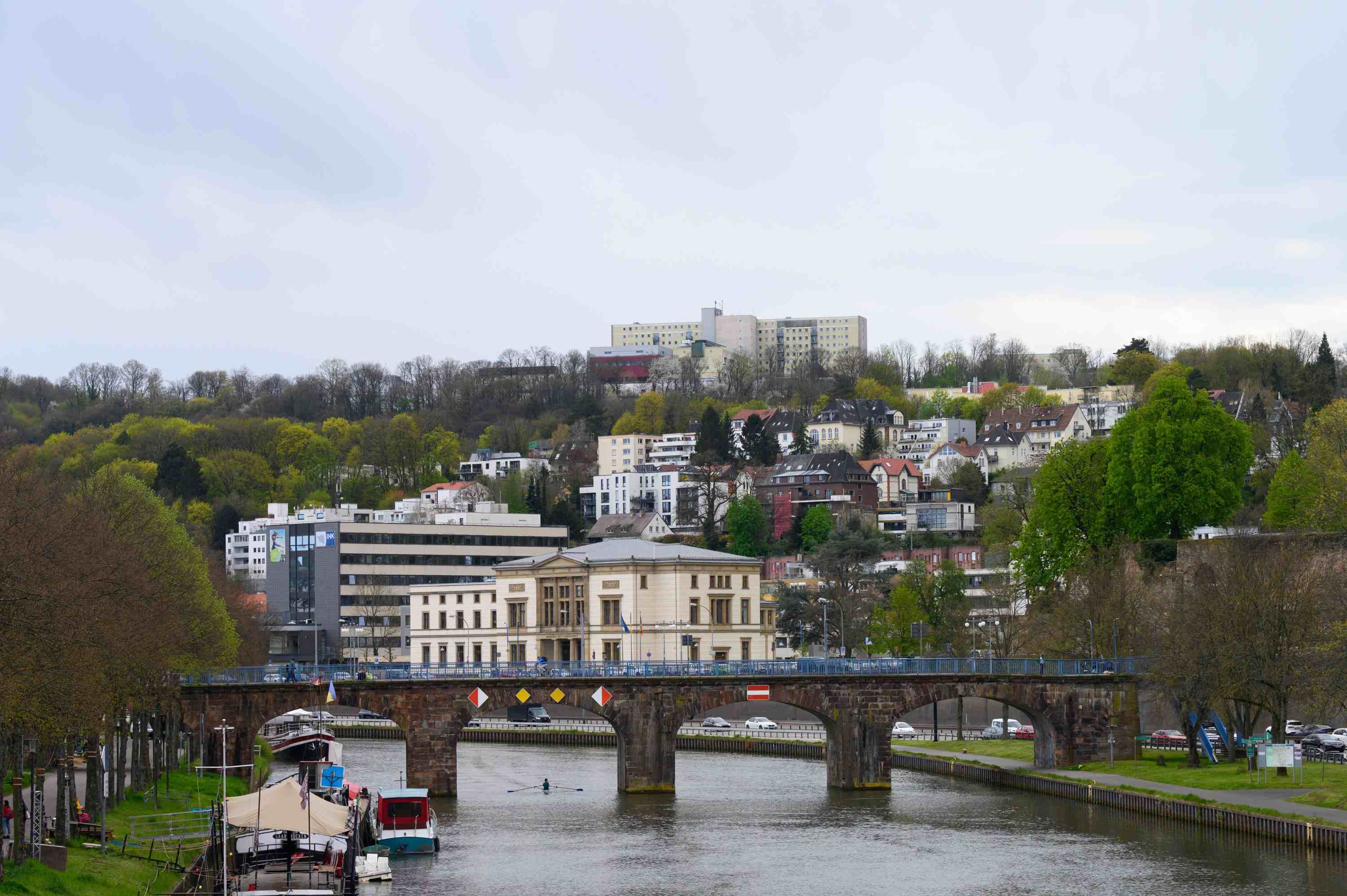 Auf dem Foto sieht man die Saar und die Alte Brücke in Saarbrücken. Im Hintergrund ist das Klinikum Saarbrücken auf dem Winterberg