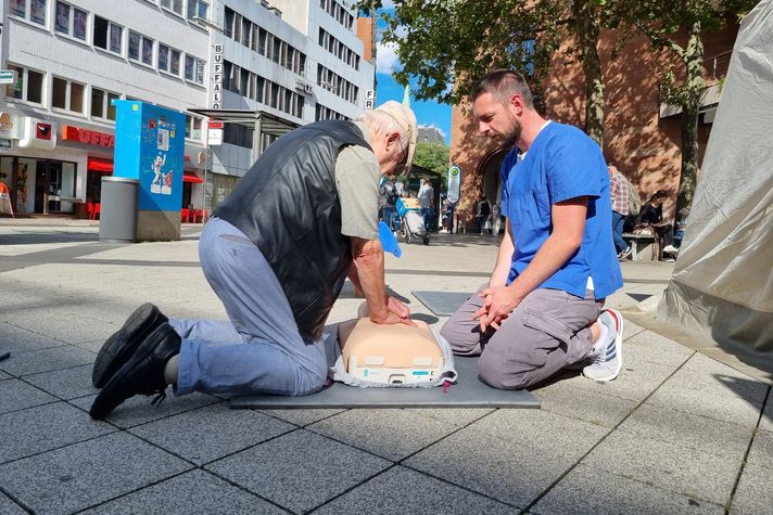 Eine Pflegekraft zeigt einem Interessierten, wie man eine Herzdruckmassage macht.