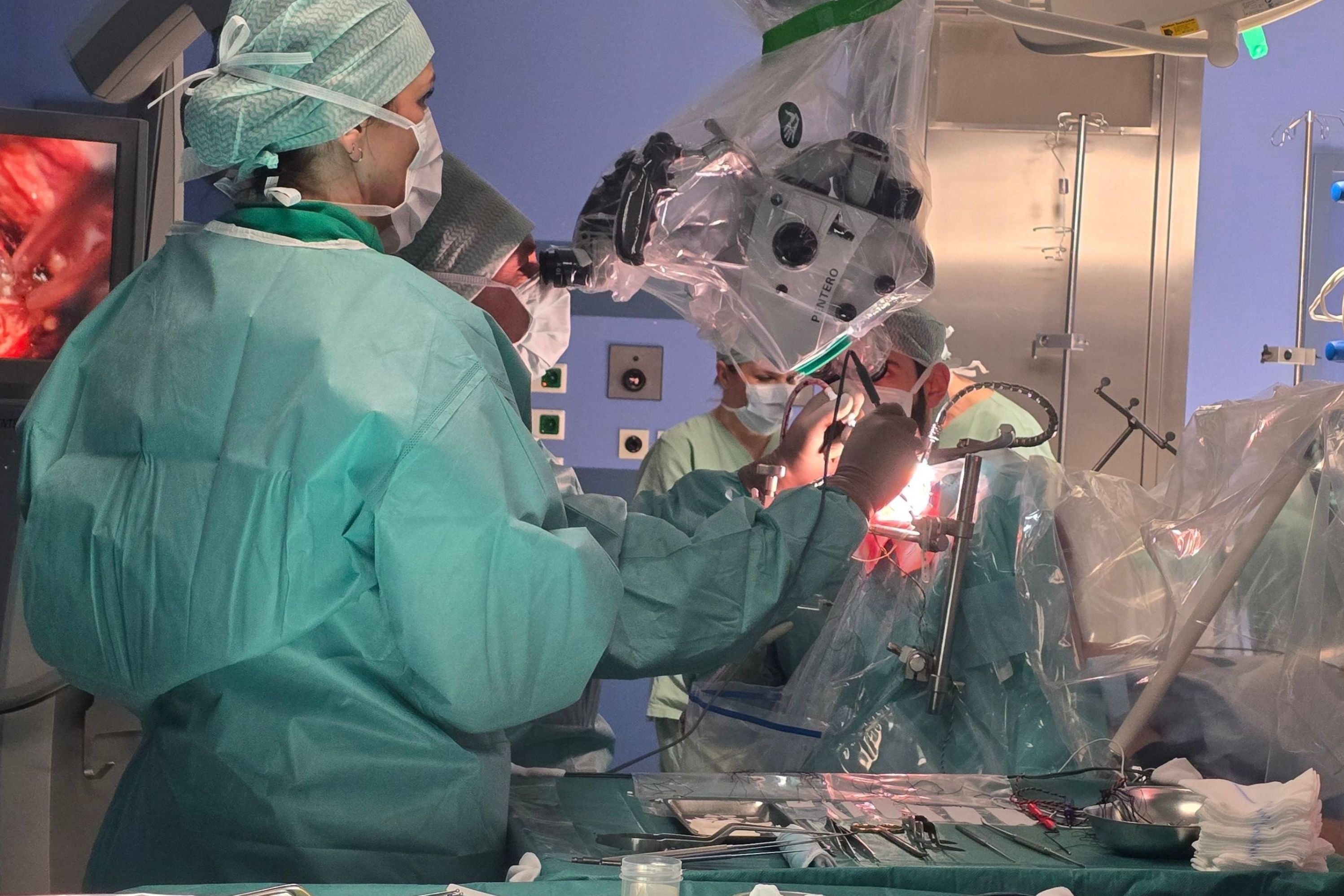 Im Operationssaal steht eine Operationstechnische Assistentin mit dem Rücken zum Zuschauer und beobachtet, was der Neurochirurg tut. 