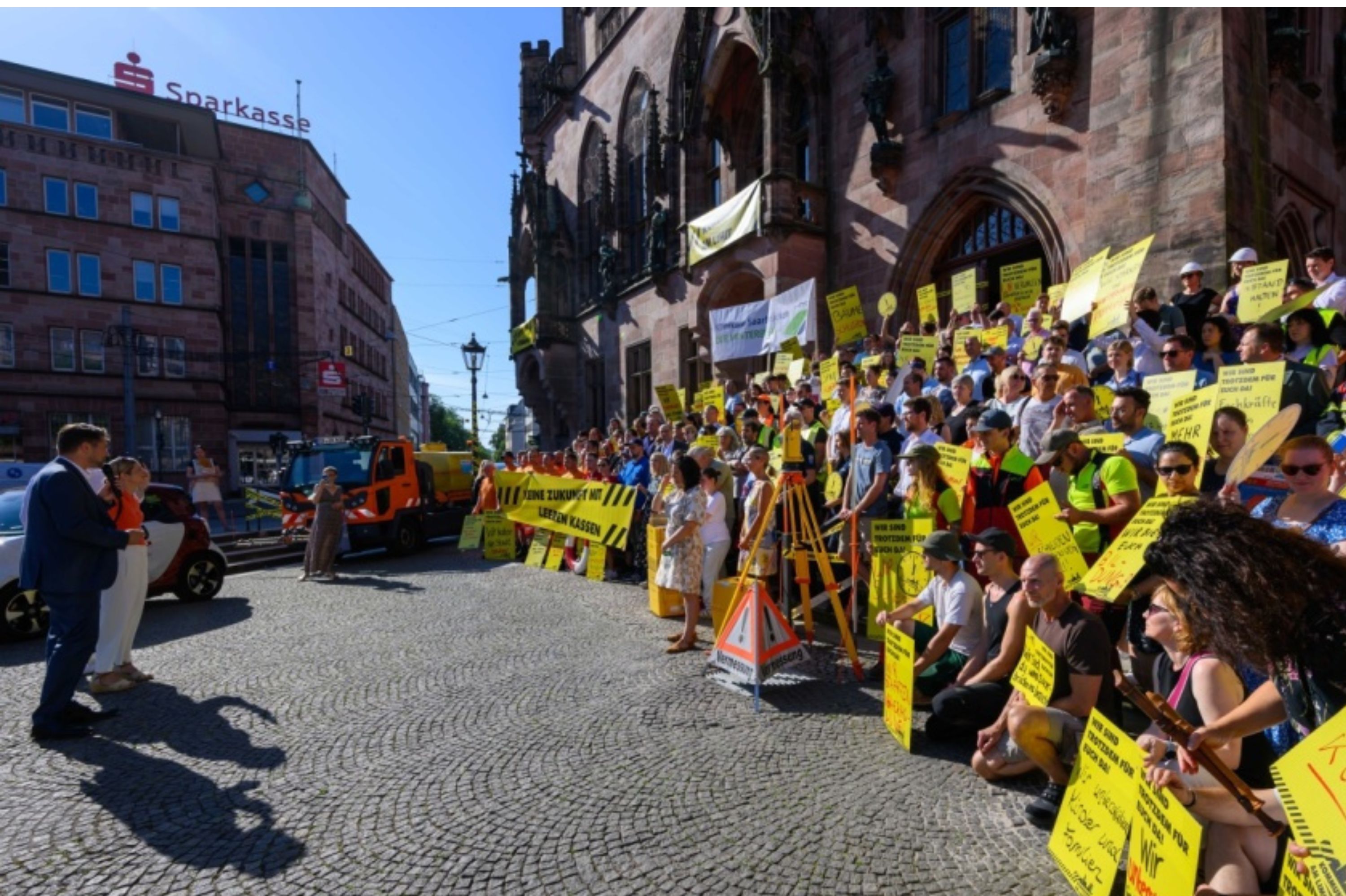 Eine Gruppe protestiert vorm Rathaus und hält Schilder hoch.
