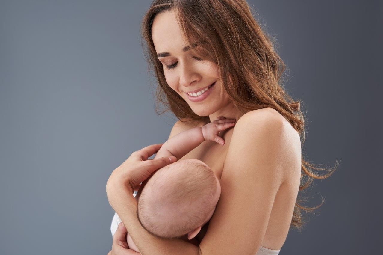 Mutter mit Baby im Arm vor grauem Hintergrund beim engen Hautkontakt und Bonding (Foto: AdobeStock_249607540)