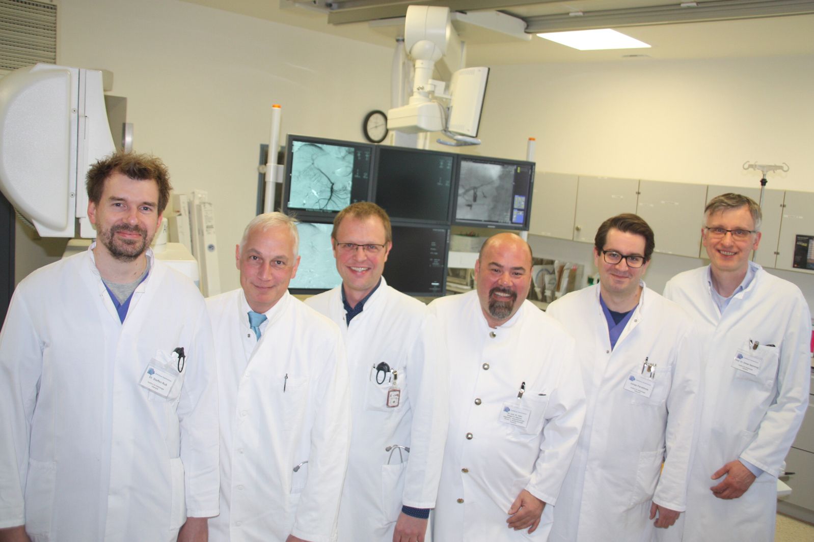 Team des Onkovaskulären Zentrums: Sechs Ärzte in Arbeitskleidung stehen aufgereiht in einem Behandlungszimmer.