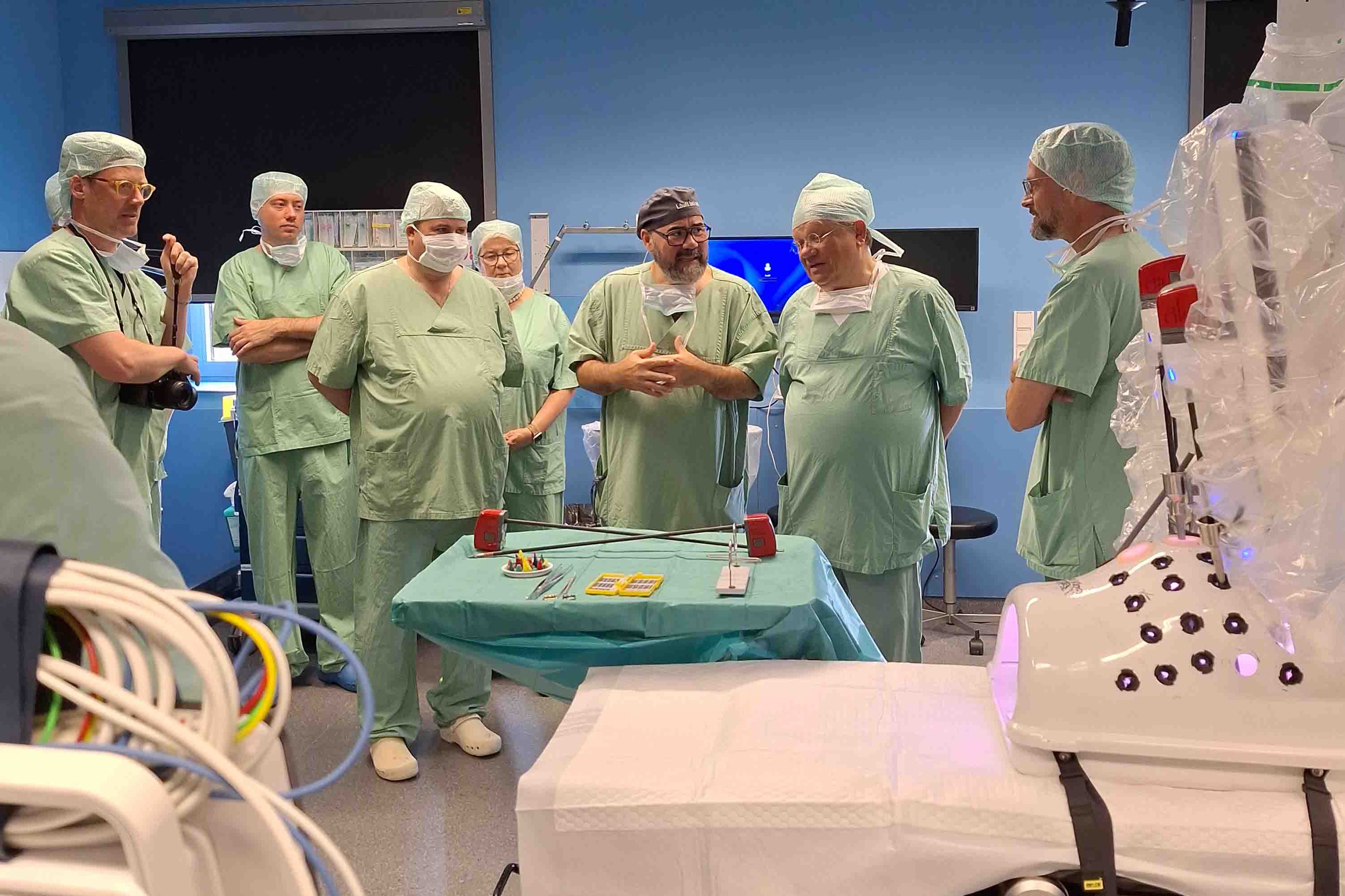 Dr. Dr. habil Stavrou erklärt Gästen in OP-Kleidung die Funktionsweise des DaVinci-Roboters.
