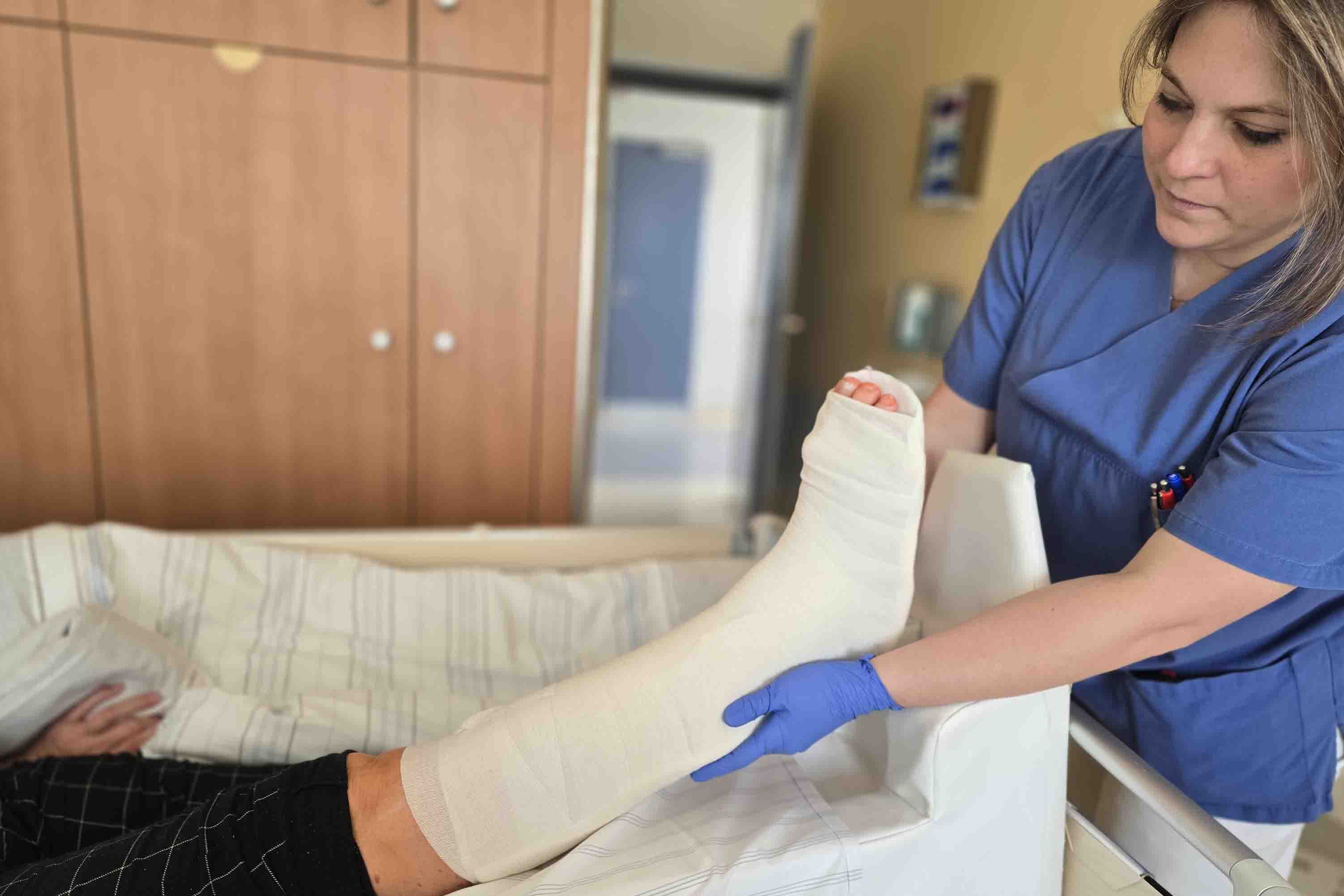 Eine Pflegekraft hebt vorsichtig das Gipsbein einer Patientin an und lagert es neu.