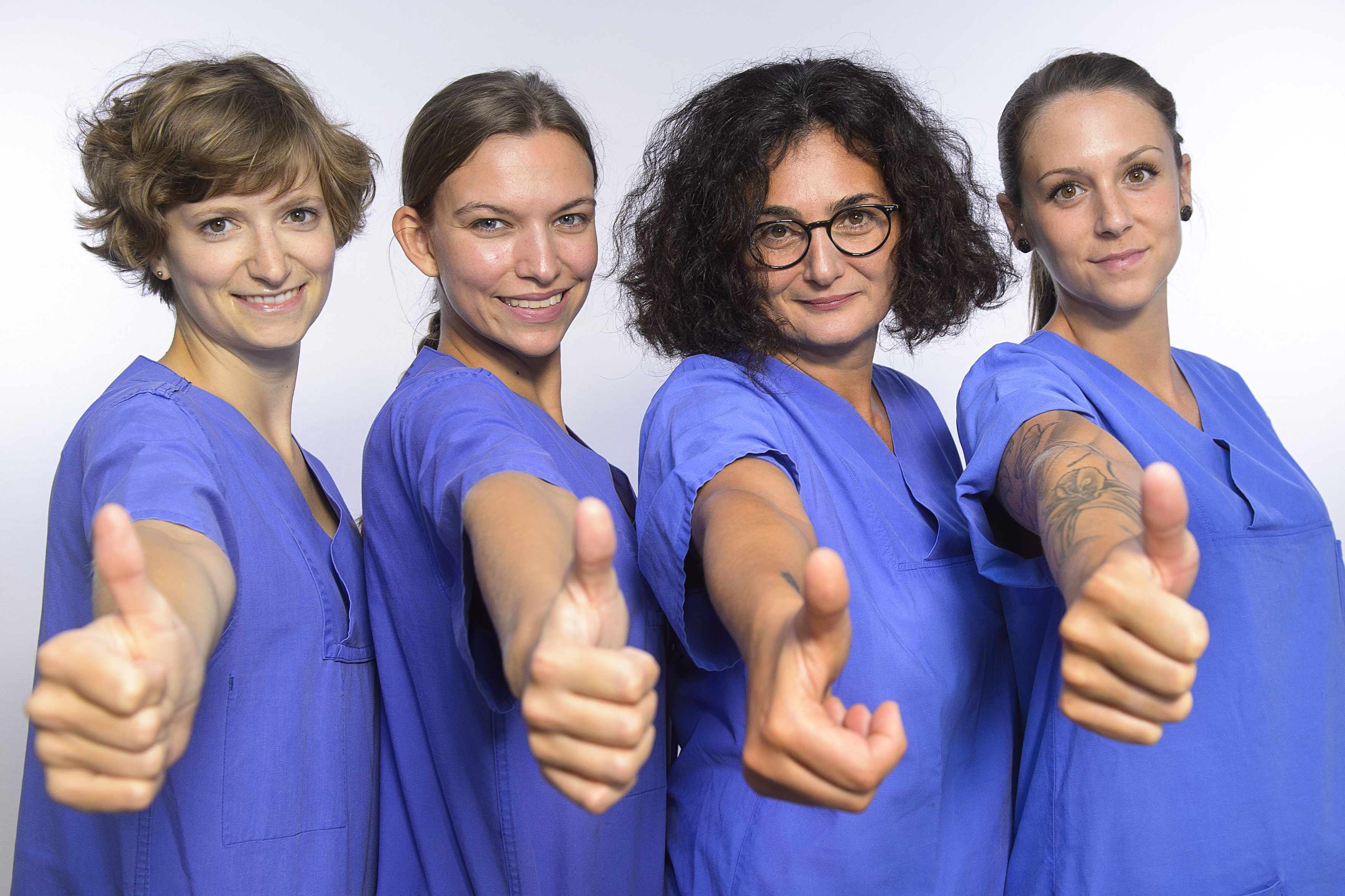Vier Frauen mit medizinischer Arbeitskleidung schauen in die Kamera und halten den Daumen hoch.