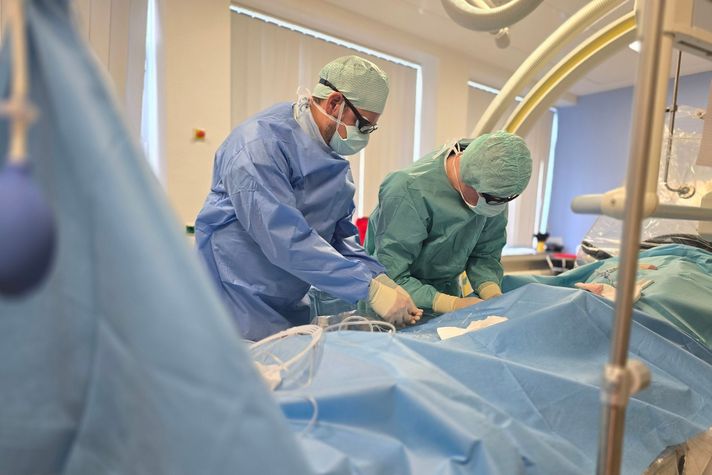 Das Bild zeigt zwei Radiologen bei einem Eingriff, sie sind steril gekleidet und behandeln einen Patienten.