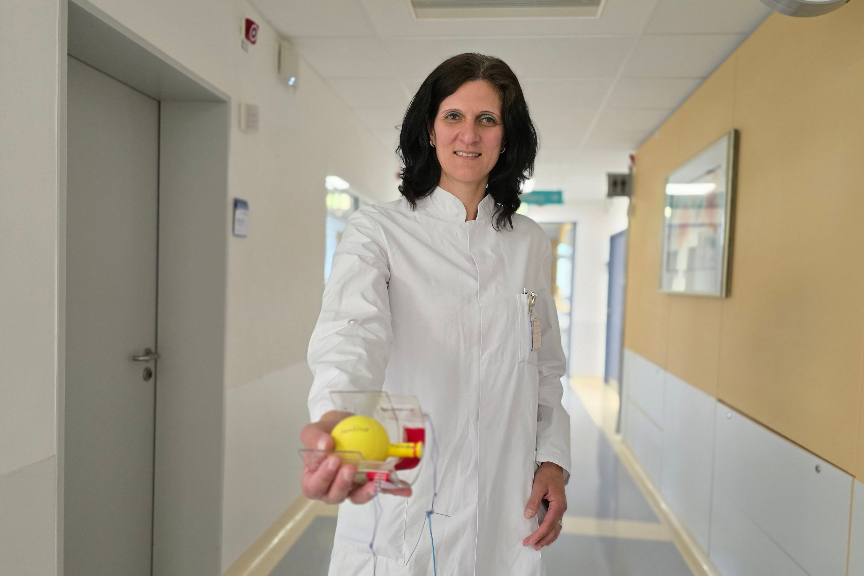 Eine Ärztin hält das Modell einer Blase in die Kamera, sie steht in einem Krankenhausflur und trägt einen weißen Kittel.