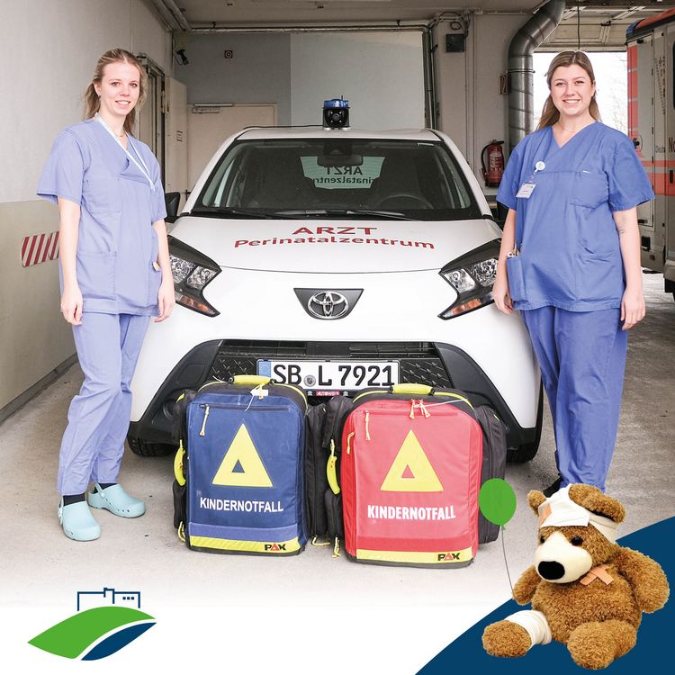Serie #TeamKiKli: KIS – Pflege, die stark macht; Kinderkrankenpflegerinnen Samira Adams und Christina Altmeyer vor dem Notfall-Fahrzeug des Perinatalzentrums auf dem Winterberg