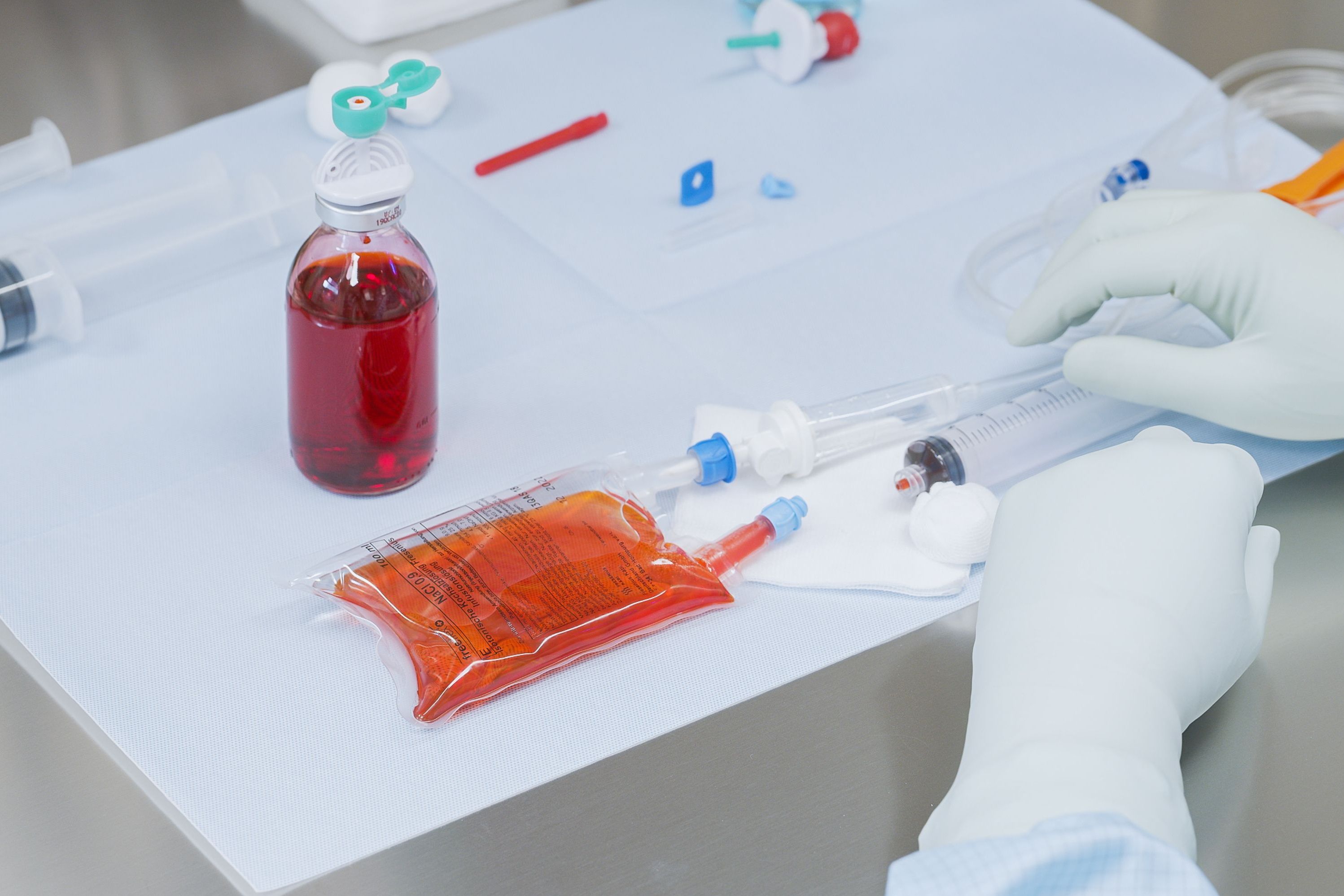 Zwei Hände in Handschuhen ziehen Flüssigkeit in eine Spritze auf.